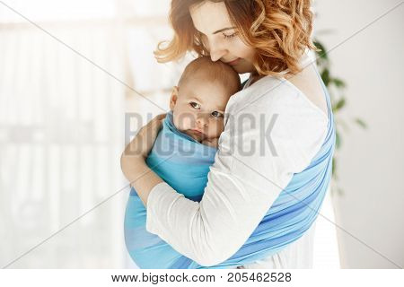 Portrait of beautiful young mother holding tight her newborn baby boy with love and caring. She smiling and feeling happiness of maternity moments