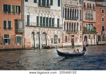 VENICE, ITALY - SEPTEMBER 2017: Gondolier rides gondola with tourists on the Grand Canal. The profession of gondolier is controlled by a guild, which issues 425 licenses