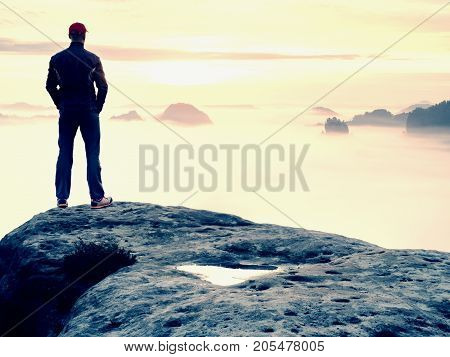 Man stands alone on the peak of rock. Hiker watching to autumn Sun at horizon . Beautiful moment the miracle of nature. Colorful mist in valley. Man hike. Person silhouette stand