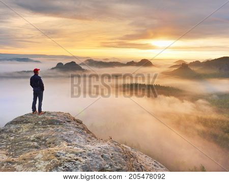 Man stands alone on the peak of rock. Hiker watching to autumn Sun at horizon . Beautiful moment the miracle of nature. Colorful mist in valley. Man hike. Person silhouette stand