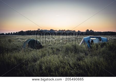 camping site with camping tents on summer rural field and sunset sky during camping holidays