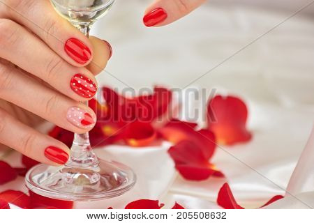 Female red manicure and champagne glass. Beautiful woman hands with gel manicured nails holding a glass of champagne. Romance and celebration concept.