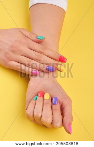 Womans hands with summer colors nails. Multicolor female manicure on yellow summer background.