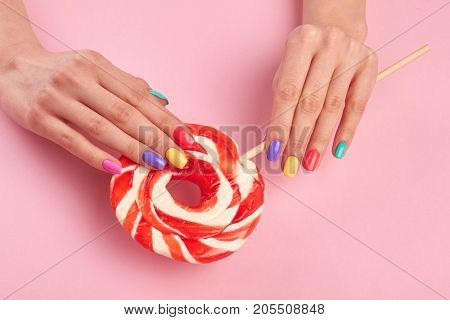 Female hands with large lollypop. Beautiful woman hands with colorful nails holding tasty lollipop on colored background.