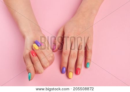 Pastel manicure on female hands. Young woman hands with colorful nail polish on pink table, top view. Nail salon and spa.