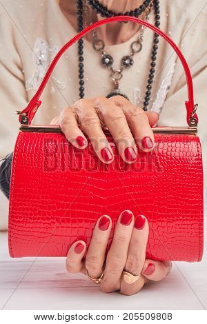 Beautiful red handbag in female hands. Woman hands with red manicure holding red leather hanbag. Female fashion accessory.