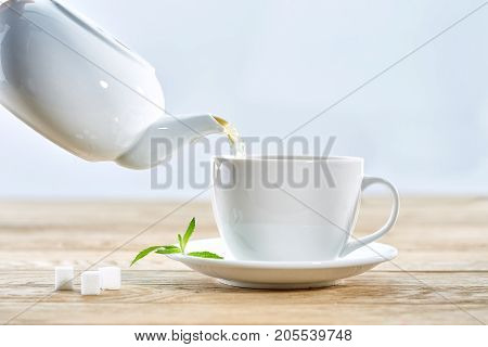 cup with green tea and teapot on white wooden table background. over light