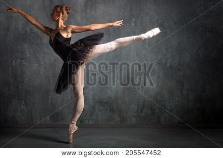 Beautiful attractive blonde woman primer ballerina in a black dance pack white pantyhose and pointe shoes beautifully dances ballet in a dark studio