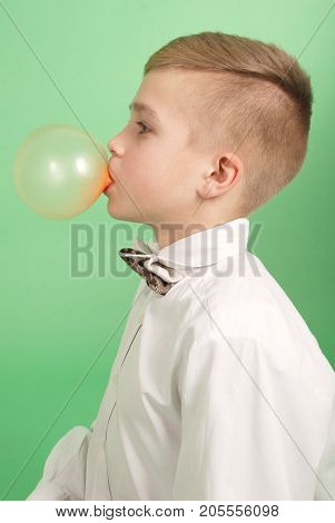 Boy blowing a bubblegum bubble isolated on green