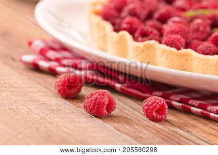 Raspberry tart with fresh rasperries in white bowl.