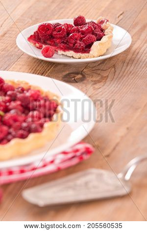 Raspberry tart with fresh rasperries in white bowl.
