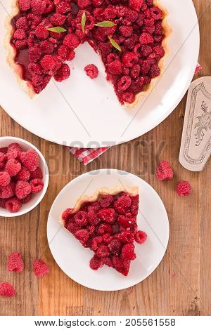 Raspberry tart with fresh rasperries in white bowl.