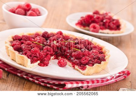 Raspberry tart with fresh rasperries in white bowl.