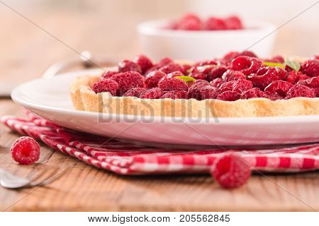 Raspberry tart with fresh rasperries in white bowl.