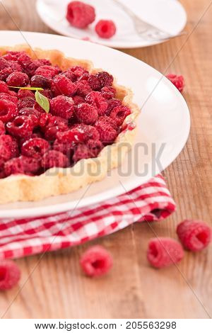 Raspberry tart with fresh rasperries in white bowl.