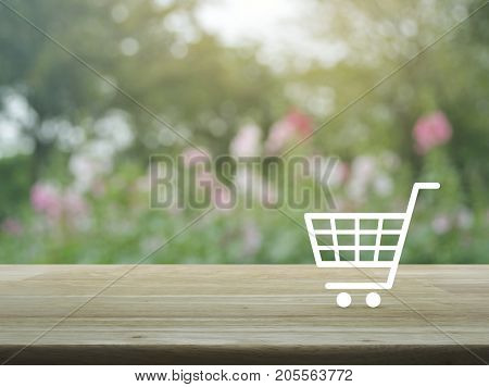 Shopping cart icon on wooden table over blur pink flower and tree Shop online concept