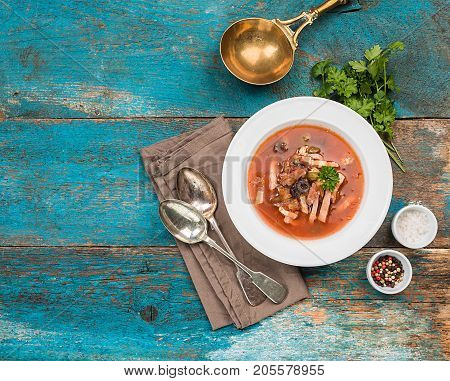 Soup with meat, olives, herbs, lemon in white bowl, black bread and spices on rustic wooden background, top view homemade food. Traditional Russian soup - solyanka