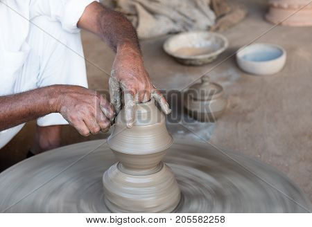 Senior man making handmade clay pottery with bare hands on the potter wheel. India handicrafts