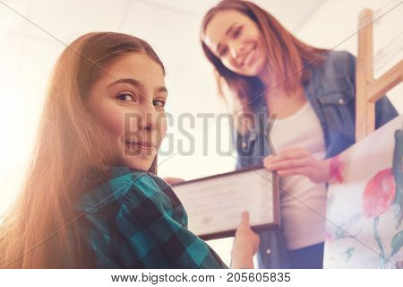 Benefits of taking additional classes. Low angle shot of a teenage lady getting excited and smiling into the camera while taking a special certificate after taking painting classes in an art workshop.