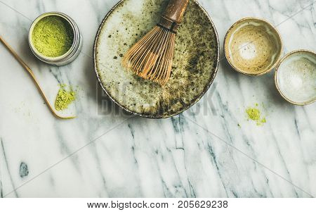 Flat-lay of Japanese tools and bowls for brewing matcha tea. Matcha powder in tin can, Chashaku spoon, Chasen bamboo whisk, Chawan bowl, cups for ceremony, grey marble background, top view, copy space