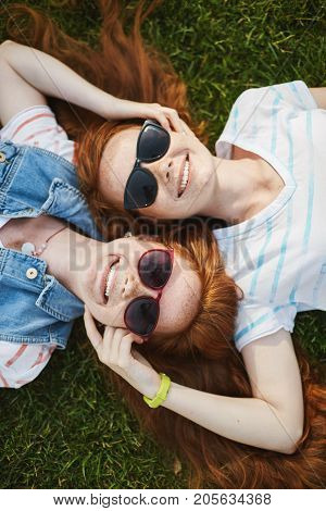 Twin ginger sisters wearing shades laying on grass on a sunny autumn day enjoying the sky. Getting grown up together in redhead madness.