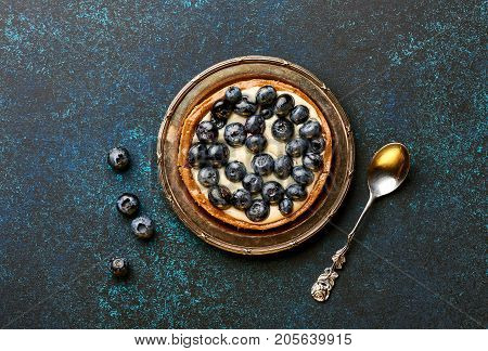 Blueberry tart, pie, tartlet with custard on blue stone background with copy space.
