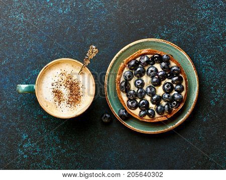 Blueberry tart with cup of coffee on blue stone background.