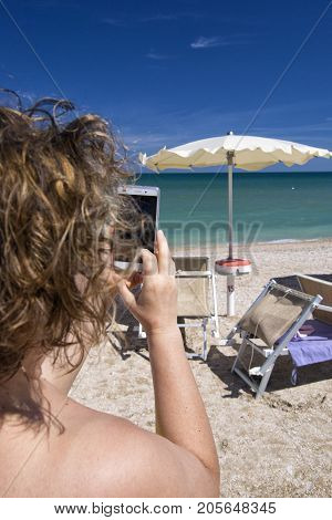 Girl looking at mobile smart phone on a beach with sea on the background. for relaxation and communication concept