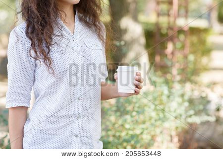 Pretty woman holding in her hands a cup of coffee on the nature. Close-up of drink.