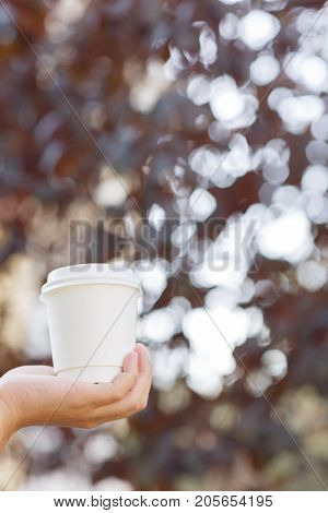 Human holding in the hand a cup of coffee on the nature. Close-up of drink.