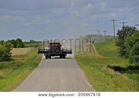 A huge self-propelled combine travels down a dirt road leaving a cloud of dust