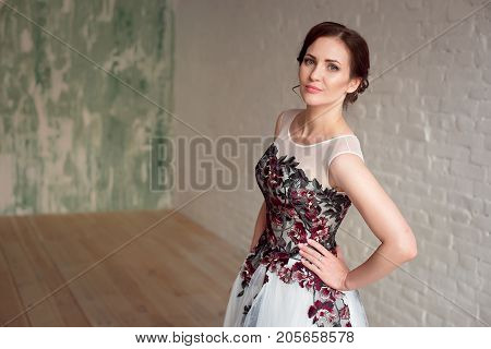 Beautiful luxurious female model with medium brown hair in a long fashinable dress standing in the room. Bridal clothes concept. Stylish wedding dress.