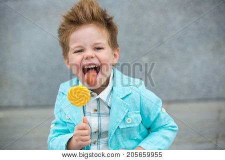Fashion baby boy in mint jacket and sneakers stands on a gray wall background. Trendy boy with lollipop standing on the street.