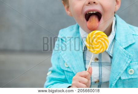 Fashion baby boy in mint jacket and sneakers stands on a gray wall background. Trendy boy with lollipop standing on the street.