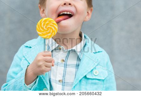 Fashion baby boy in mint jacket and sneakers stands on a gray wall background. Trendy boy with lollipop standing on the street.