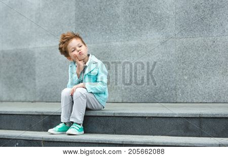 Fashion baby boy in mint jacket and sneakers posing on a gray wall background. Trendy boy standing on the street.