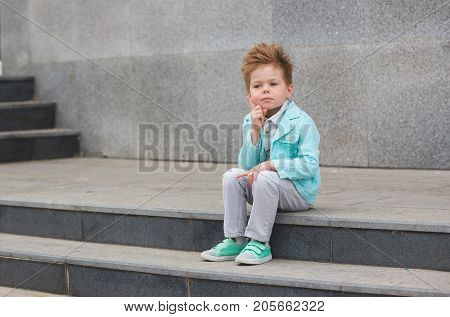 Fashion baby boy in mint jacket and sneakers posing on a gray wall background. Trendy boy standing on the street.