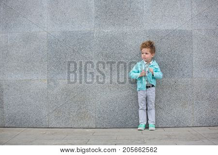 Fashion baby boy in mint jacket and sneakers posing on a gray wall background. Trendy boy standing on the street.