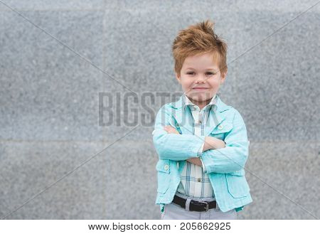 Fashion baby boy in mint jacket posing on a gray wall background. Trendy boy standing on the street.