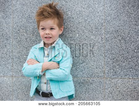 Fashion baby boy in mint jacket posing on a gray wall background. Trendy boy standing on the street.