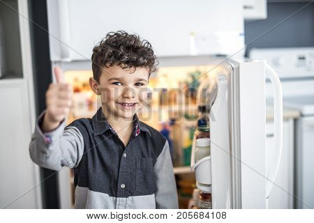 A Young white boy standing in front of open refrigerator.