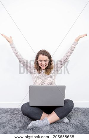 Closeup portrait of cheerful middle-aged beautiful woman working on laptop, spreading arms and sitting with her legs crossed on floor at home. Front view.