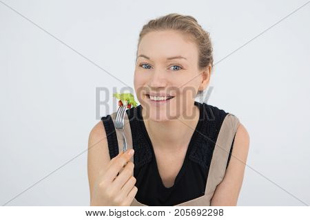 Happy attractive woman eating fresh salad and enjoying healthy lifestyle. Portrait of cheerful lady holding fork and smiling at camera. Vegan concept