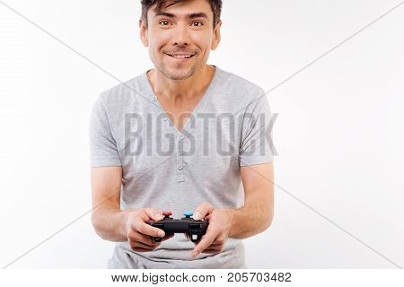 Excited gamer. Beautiful upbeat young man in a grey t-shirt holding a video game controller and looking excited about the game