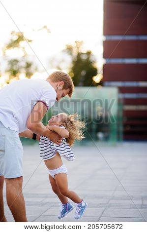 Young dad is playing with a charming little daughter. The man is holding the baby by the handles.. The child rejoices.