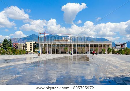 TIRANA ALBANIA - SEPTEMBER 6 2017: Unknown people ride bicycles and walk along Skanderbeg Square near National Opera and Ballet Theater of Albania Tirana