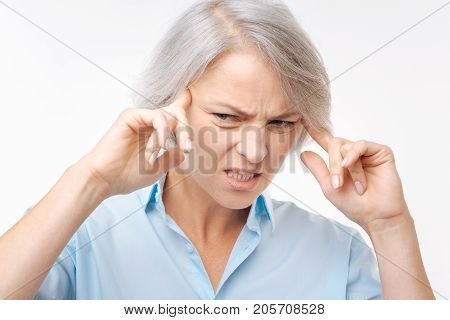 Throbbing pain. Irritated young woman pressing her fingers to the temples and suffering from a splitting headache while wincing