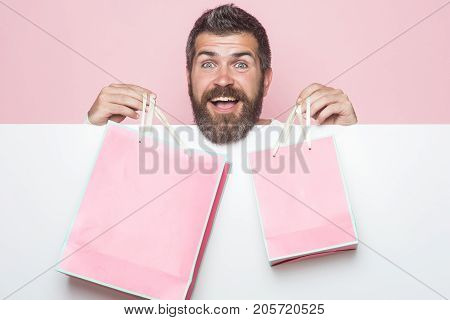 Christmas and birthday. Hipster with present package on pink background. Guy with happy face and gift pack. Man with long beard with pink shopping bag. Holiday celebration and black friday shopping.