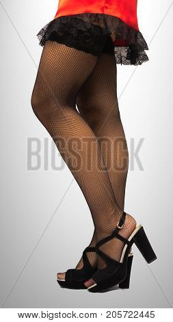 Young woman in short red dress high heel shoes and black sexy fishnet pantyhose stockings on her legs standing on the floor isolated.