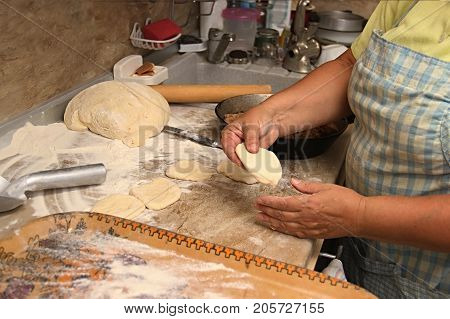 Senior woman baking pies in her home kitchen.Grandma cooks pies. Home cooked food. omemade mold cakes of the dough in the women's hands. The process of making pie dough by hand.